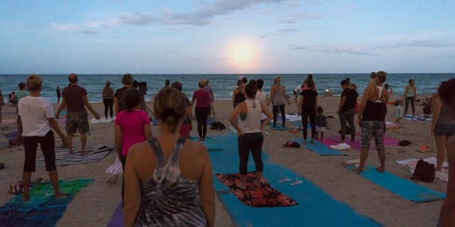 Residents practicing yoga on the beach as the full moon rises over the ocean.