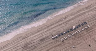 Aerial view of the neatly grated beach and shoreline with white beach chairs lined up.
