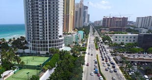 Traffic on Collins Avenue in Sunny Isles Beach with buildings and ocean view of coastline.