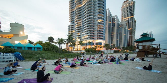 Yoga participants stretching to the side as they sit on yoga mats during class on the beach.