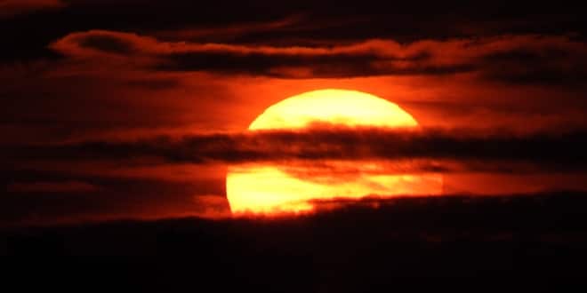 Image of the sun behind the clouds creating a red sky