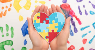 woman holding heart with puzzle on white with hand prints for World Autism Awareness