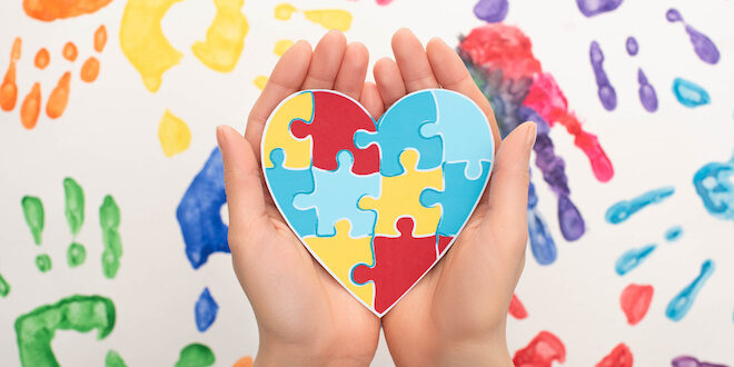 woman holding heart with puzzle on white with hand prints for World Autism Awareness