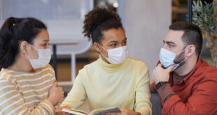 Group of people wearing masks while working at a table together in a cafe.