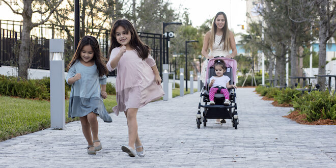 Mom pushes stroller as two young girls run ahead on sidewalk at Gateway Park