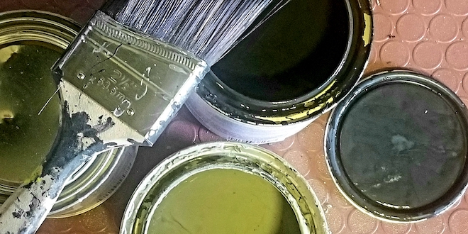 Paints cans containing black and green paint with a paint brush laying on top.